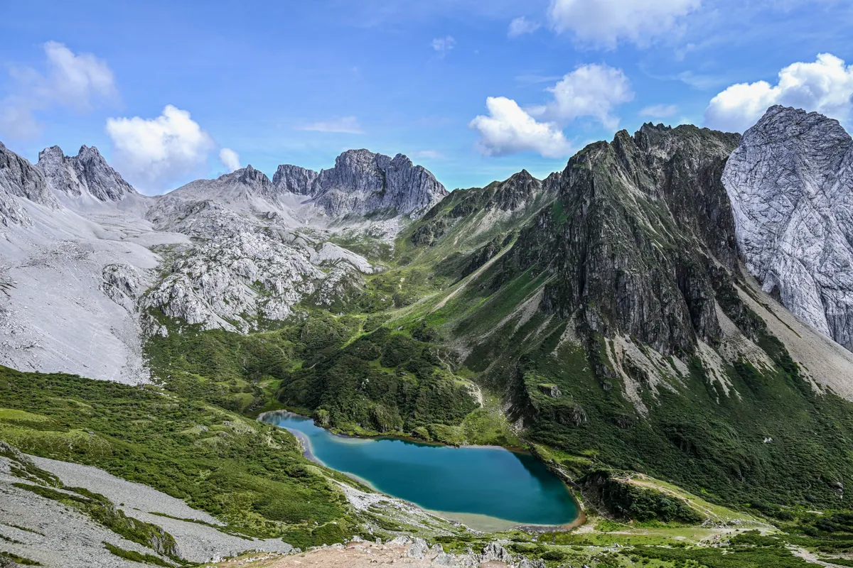 A turquoise alpine lake surrounded by rugged peaks and green slopes.