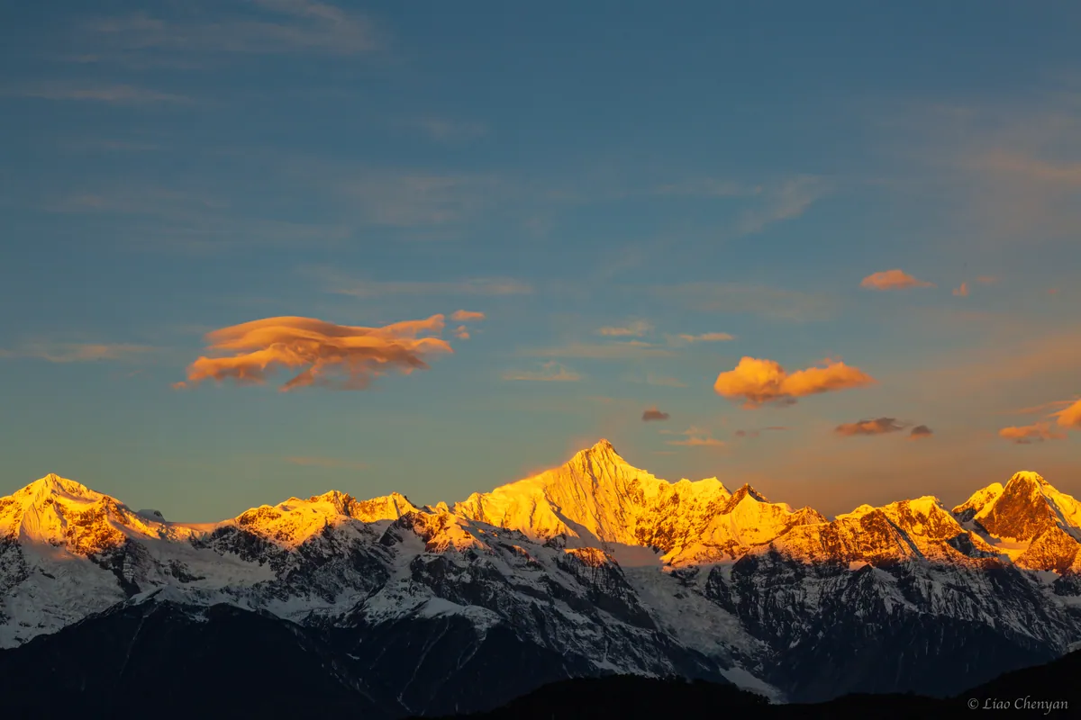 Golden sunrise illuminating a high mountain ridge above dark blue valleys.